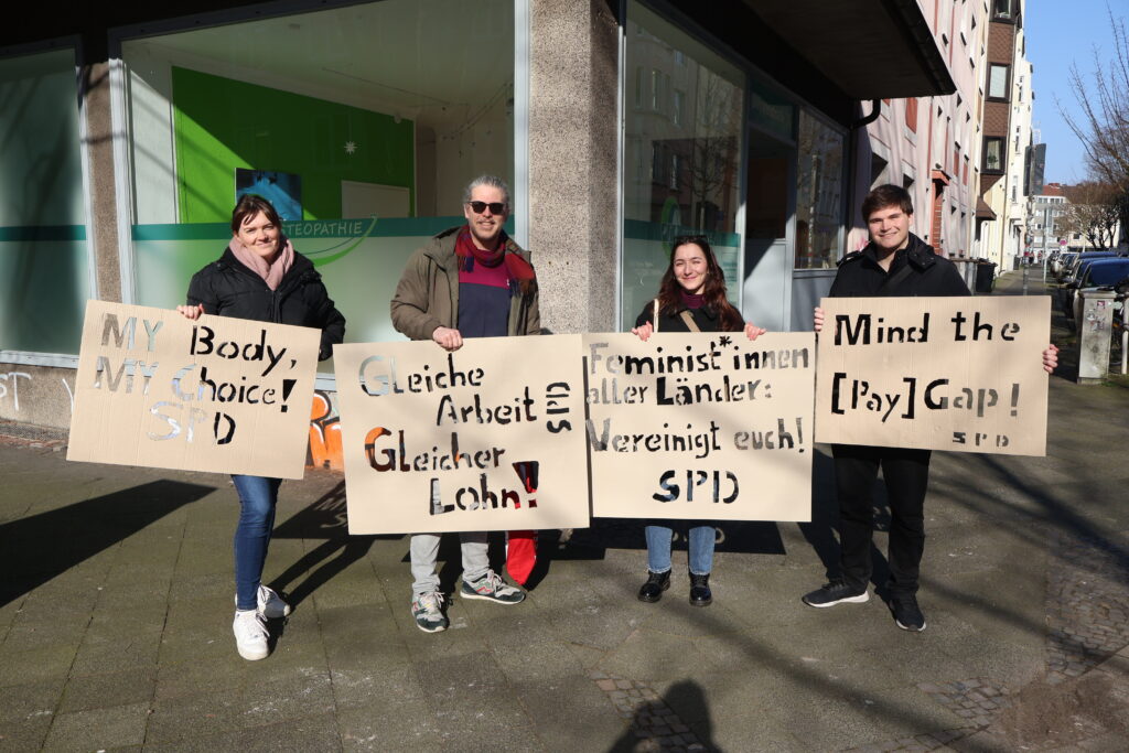 Vier Personen halten Schilder mit feministischen Forderungen in den Händen.